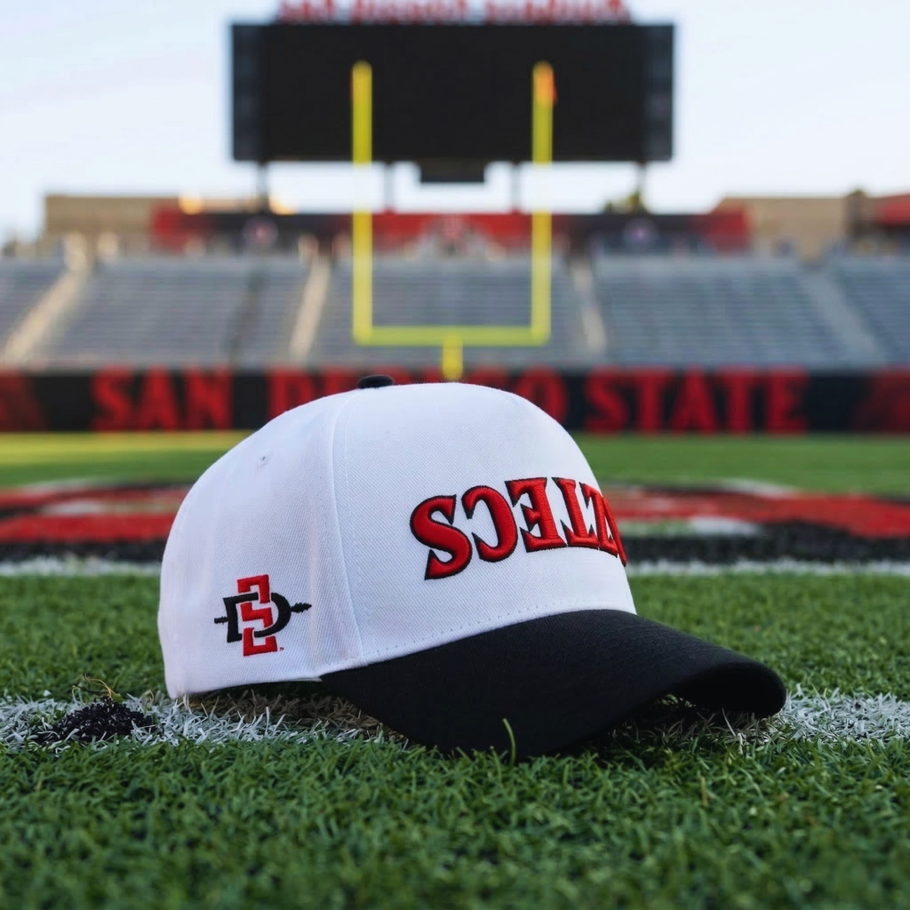 White and black cap with 'Aztec' upside down on a football field