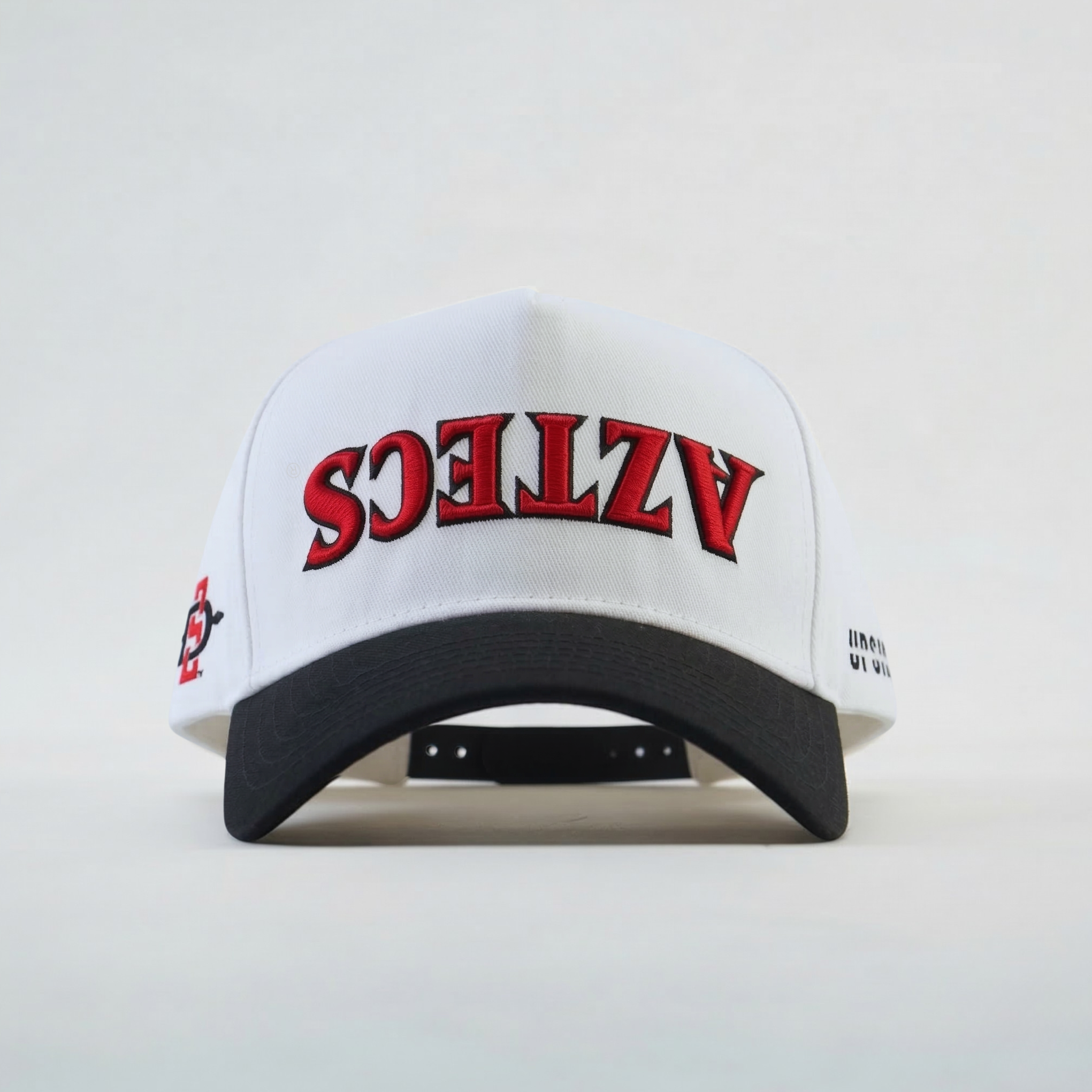White cap with red and black "Aztec" upside down text on a light gray background