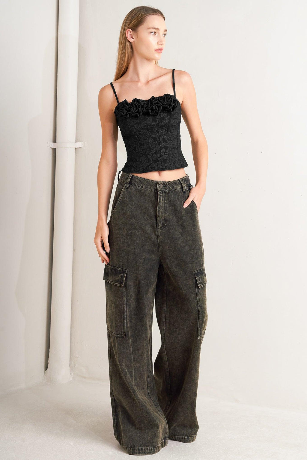 Woman wearing a black ruffled top and dark green cargo pants on a white background