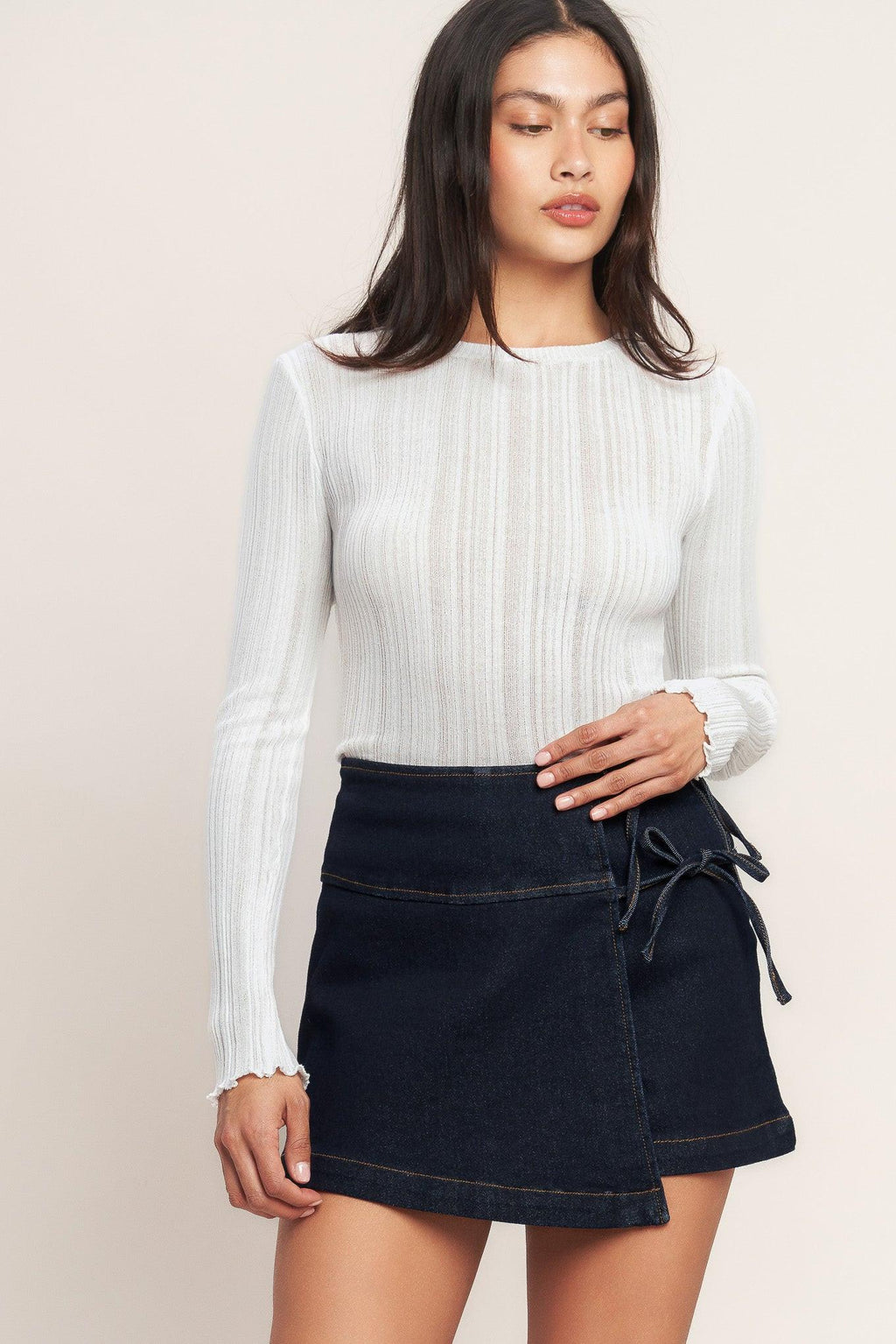 Woman wearing a white ribbed sweater and black denim skirt on a beige background