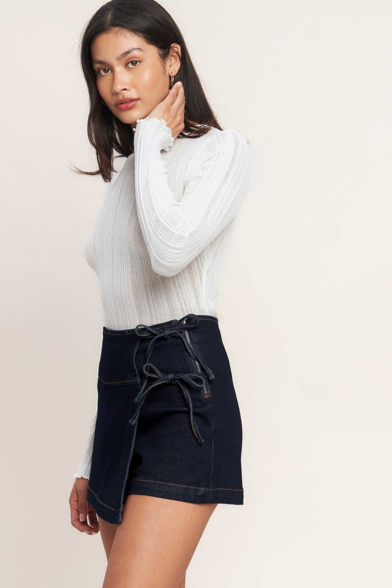 Woman wearing a white ribbed sweater and black denim skirt on a beige background