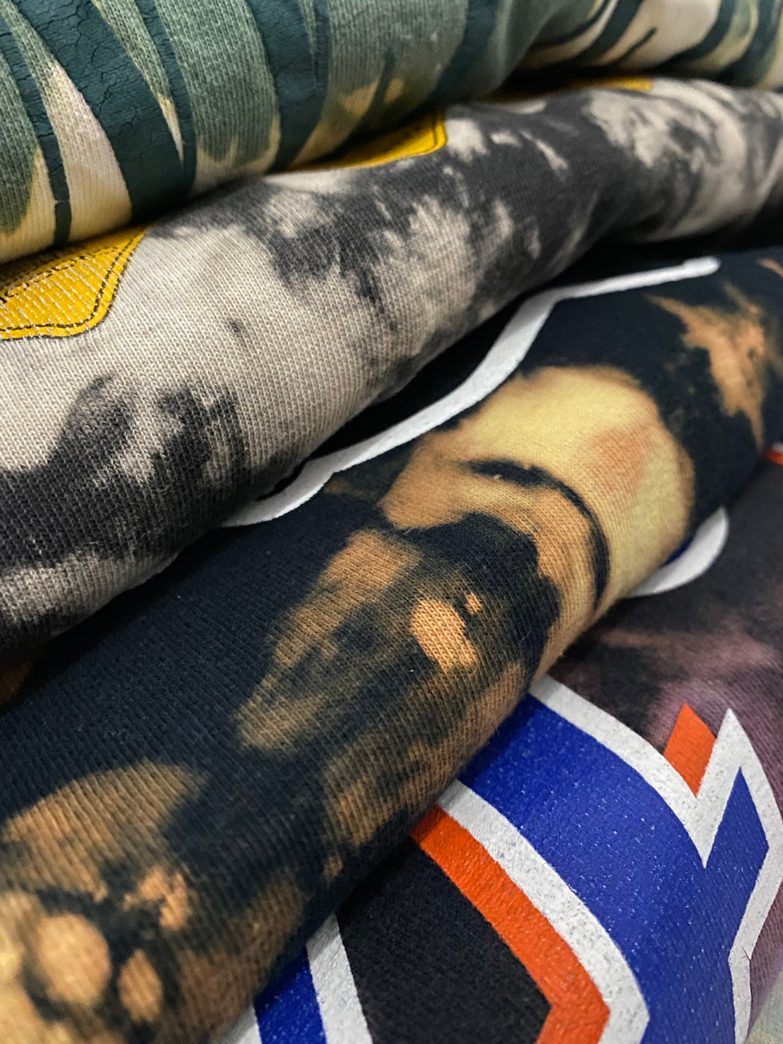 Stack of patterned fabrics including camouflage and abstract designs.