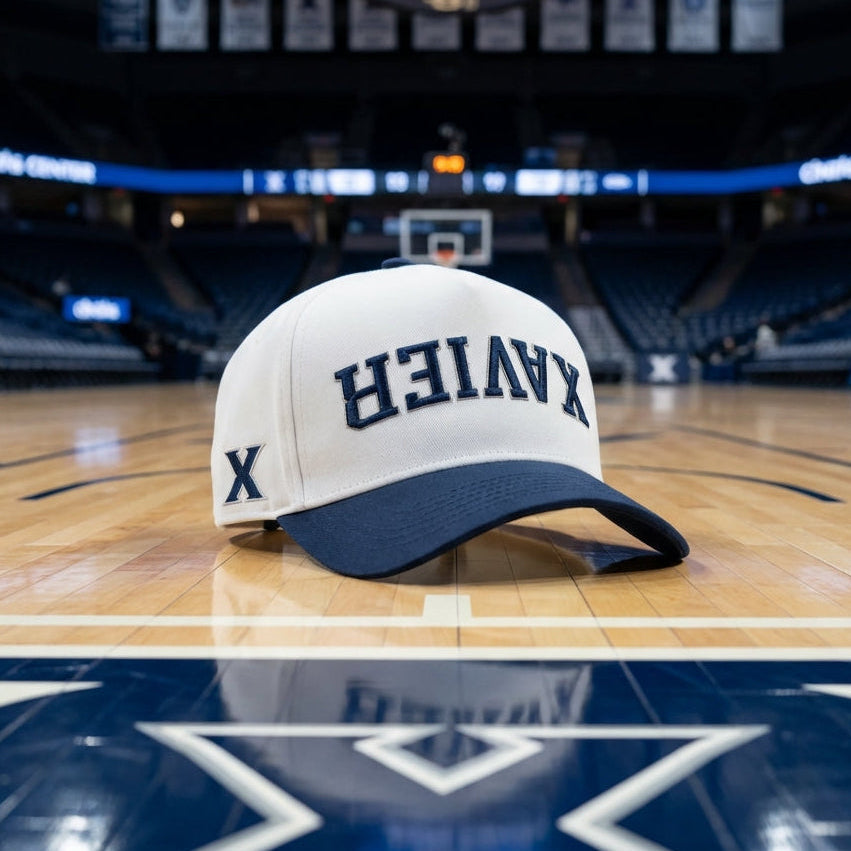 White and blue cap with 'XAVIER'  upside down branding on a basketball court