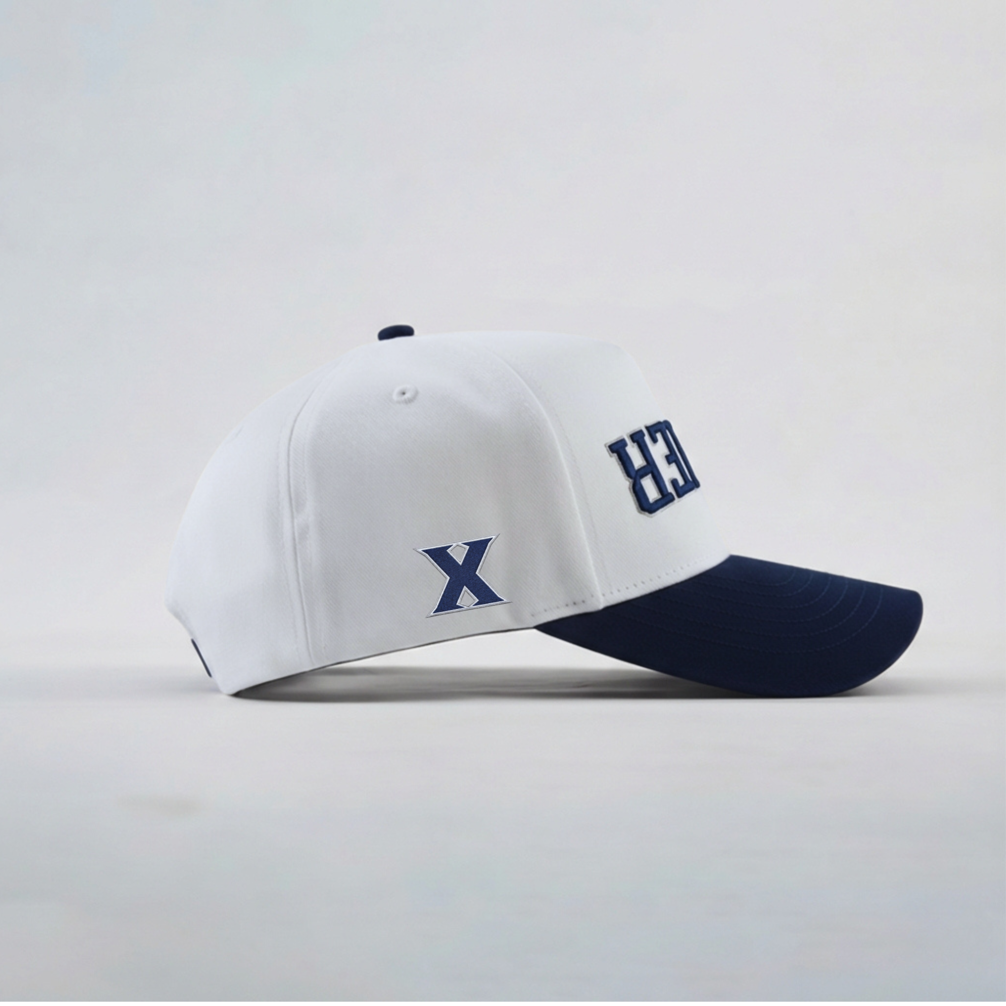 White and navy baseball cap with 'X' logo on a light gray background